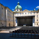 Concert în aer liber într-o piață istorică plină de oameni, cu clădiri vechi luminate seara