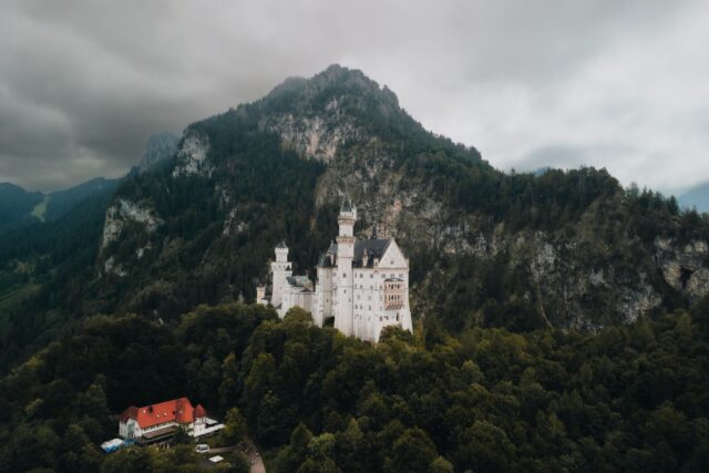Castel în stil neorenascentist înconjurat de pădure de brazi, la poalele munților, într-o zi senină