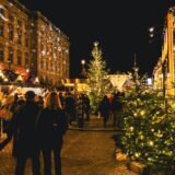 Căsuțe de lemn luminate ale unui târg de Crăciun într-o piață istorică, seara, cu un brad mare împodobit în centru