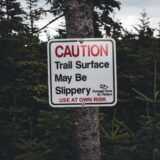 Potecă de pădure la munte, cu un indicator de avertizare fixat pe un copac la marginea traseului