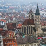 Turnul unei biserici gotice deasupra acoperișurilor roșii ale centrului vechi al Brașovului, cu muntele în fundal