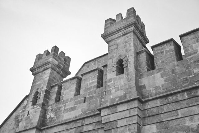Bastion medieval din piatră cu acoperiș înalt din lemn, lângă zidurile vechi ale cetății, la poalele unui deal împădurit